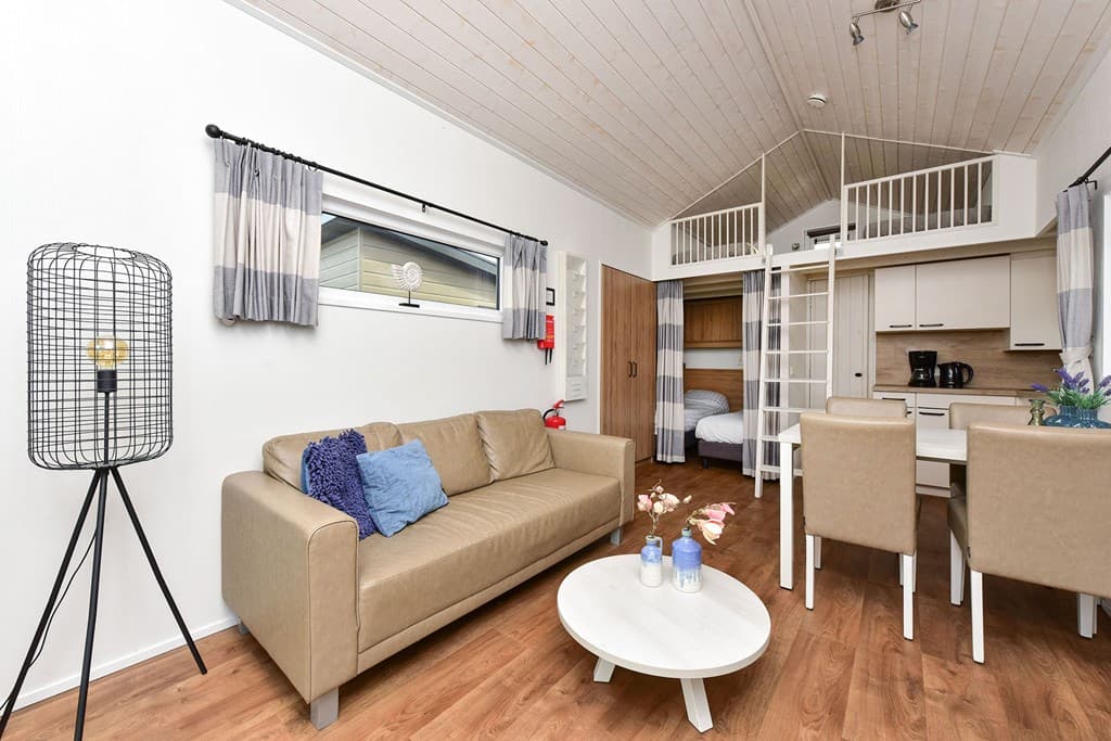 Woonruimte met een bank, tafel, kitchenette en bovenverdieping met een slaapgedeelte en ladder.