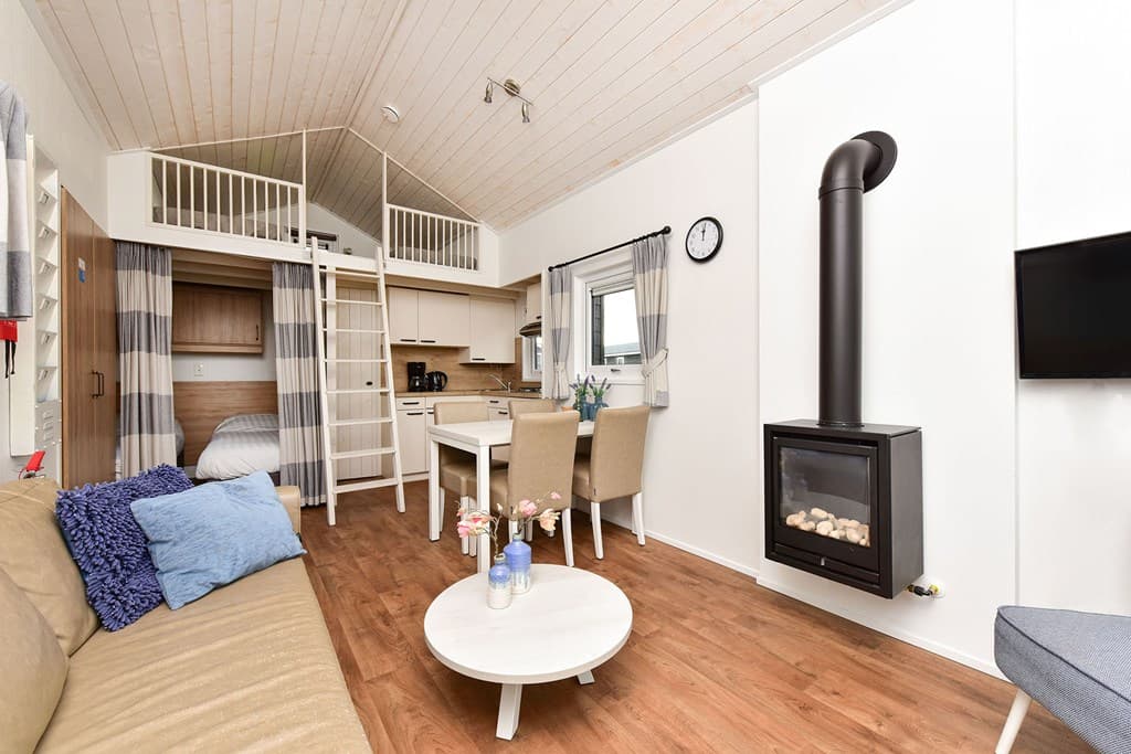 Interieur van een vakantiewoning met zithoek, eettafel, open keuken en een vide met slaapkamer boven.