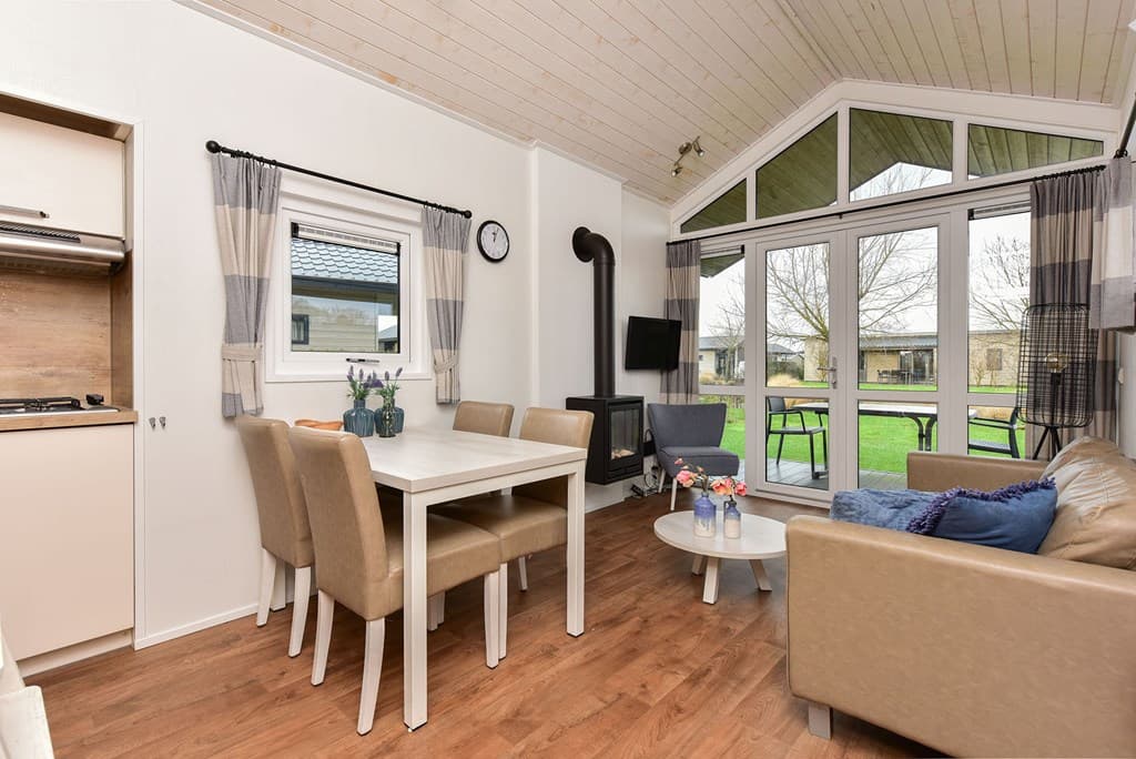 Zithoek met bank en TV, eettafel met stoelen, grote ramen met uitzicht op de tuin en omgeving.
