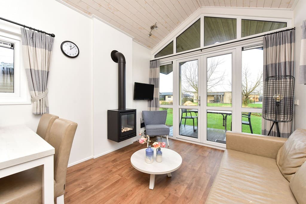 Lichte woonkamer met zithoek, eettafel en grote ramen met uitzicht op de tuin en buitenruimte.