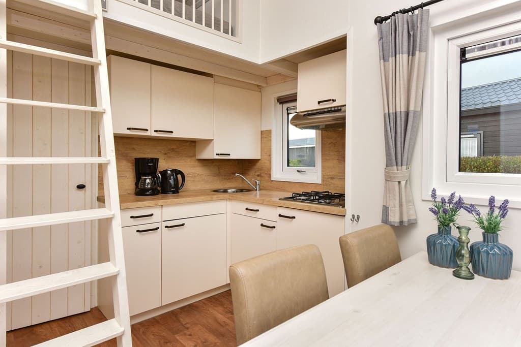 Keuken met houten planken, witte kastjes, gasfornuis en een eettafel met stoelen, naast een trap naar de bovenverdieping