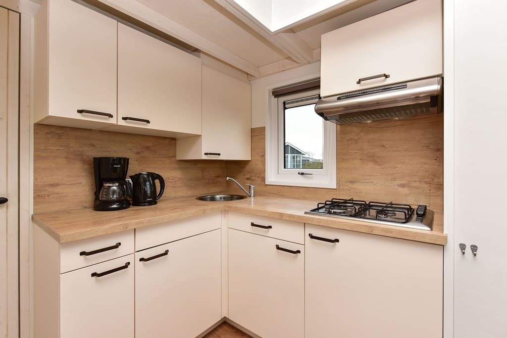 Keuken met lichte kasten, houten werkblad, gaskookplaat, afzuigkap en koffiezetapparaat in vakantiehuis.