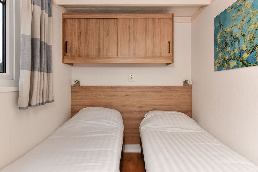 Slaapkamer met twee eenpersoonsbedden, houten wandmeubel en een schilderij aan de muur