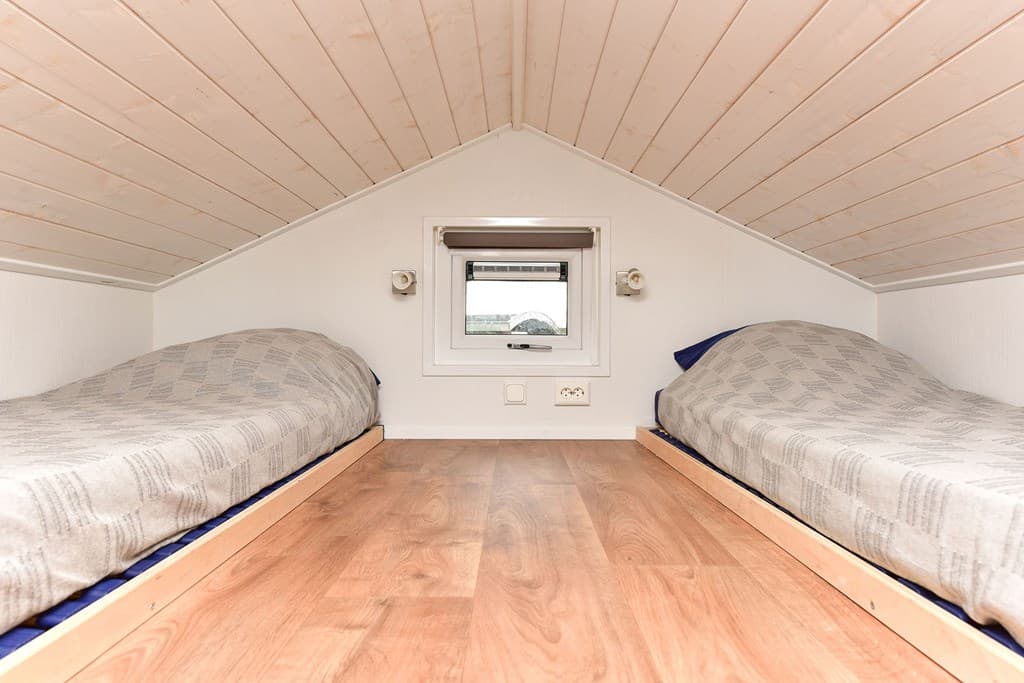 Slaapzolder met twee eenpersoonsbedden en een klein raam, houten vloer en schuin plafond.
