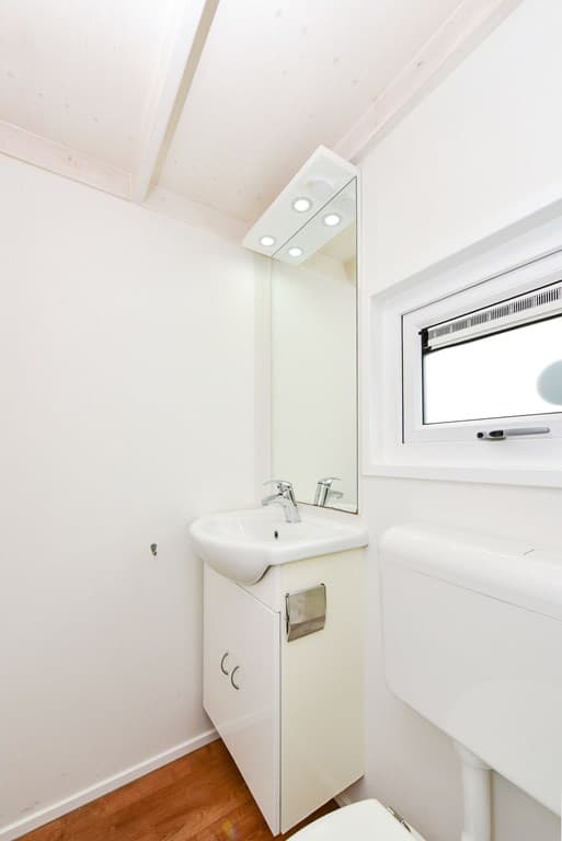 Toiletruimte met wastafel, spiegel en raam, eenvoudig ingericht met lichte wanden en houten vloer