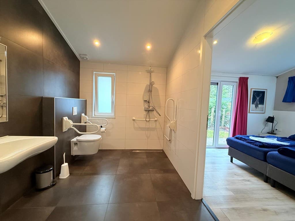 Ruime badkamer met inloopdouche, toilet en wastafel, toegang naar slaapkamer met twee enkele bedden en raam met zicht op de t