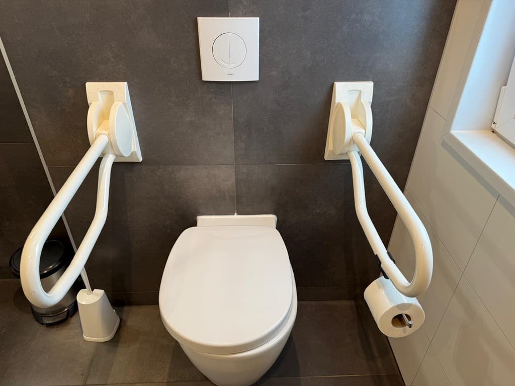 Toilet met muursteunen en toiletrolhouder, moderne tegelwand en een eenvoudig design.