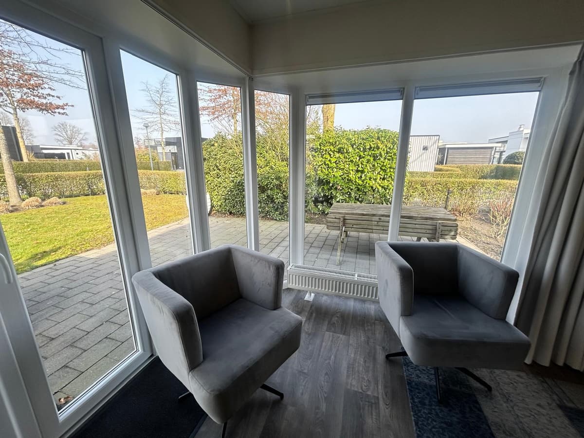 Zitruimte met twee grijze stoelen en uitzicht op een betegelde tuin met bank en groenstrook