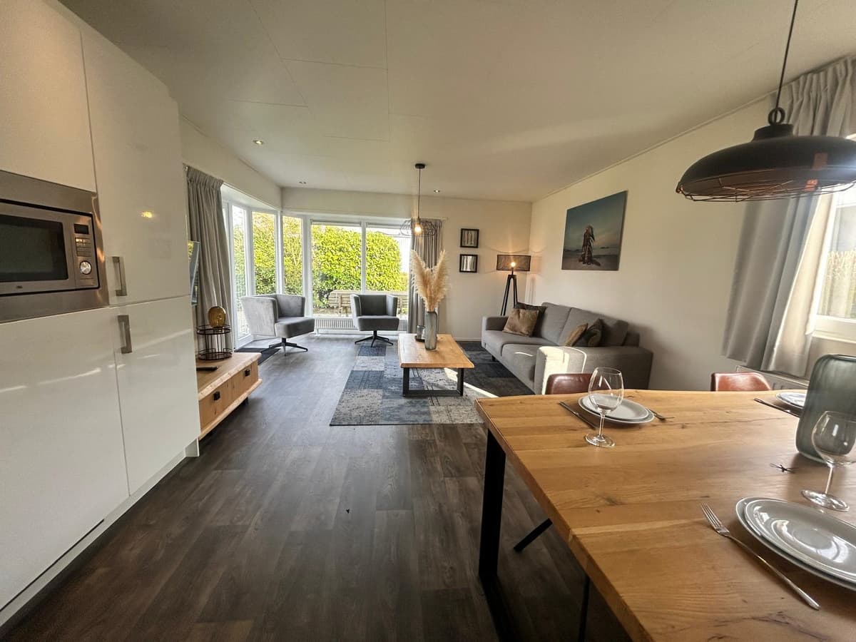 Moderne woonkamer met zithoek, eettafel en grote raampartij voor natuurlijk licht.