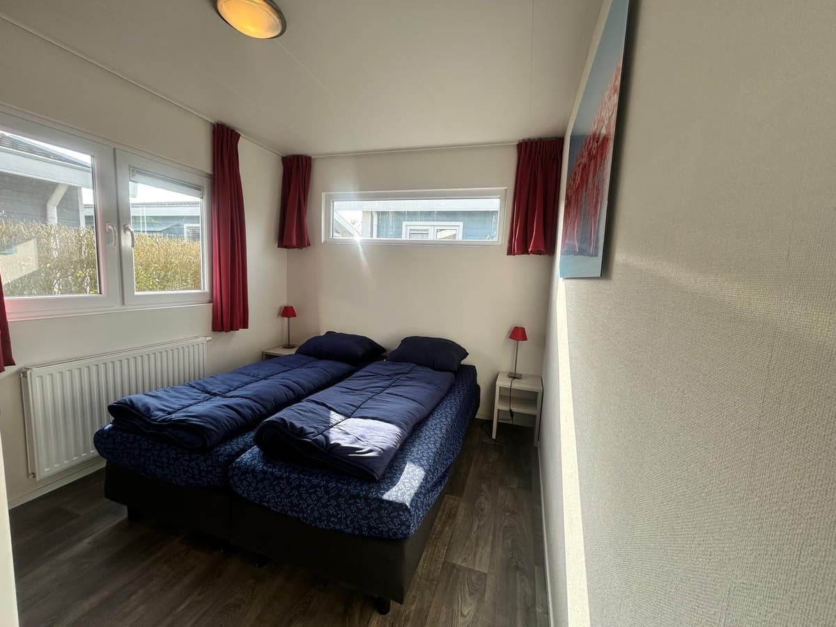Slaapkamer met twee enkele bedden, ramen met natuurlijk licht en rode gordijnen.