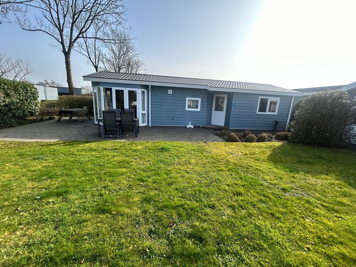 Buitenzijde van een chalet met een terras en zwarte tuinmeubelen, omgeven door gras en struiken