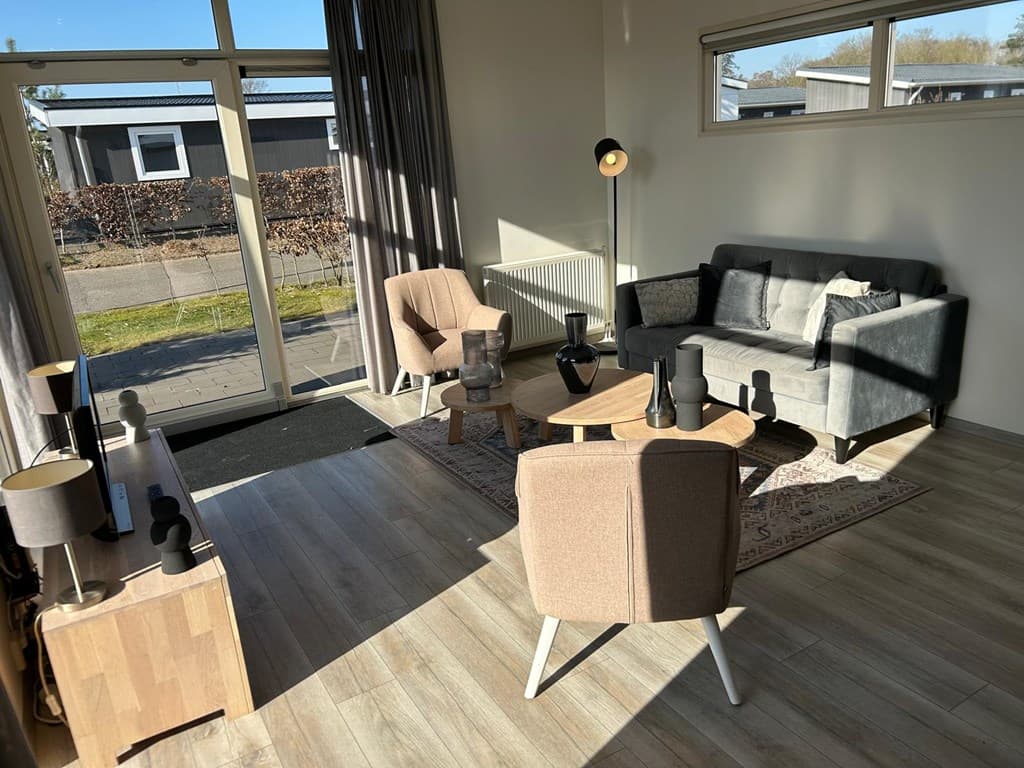 Woonkamer met grote ramen, comfortabele meubels en een moderne inrichting in EuroParcs Veluwemeer.