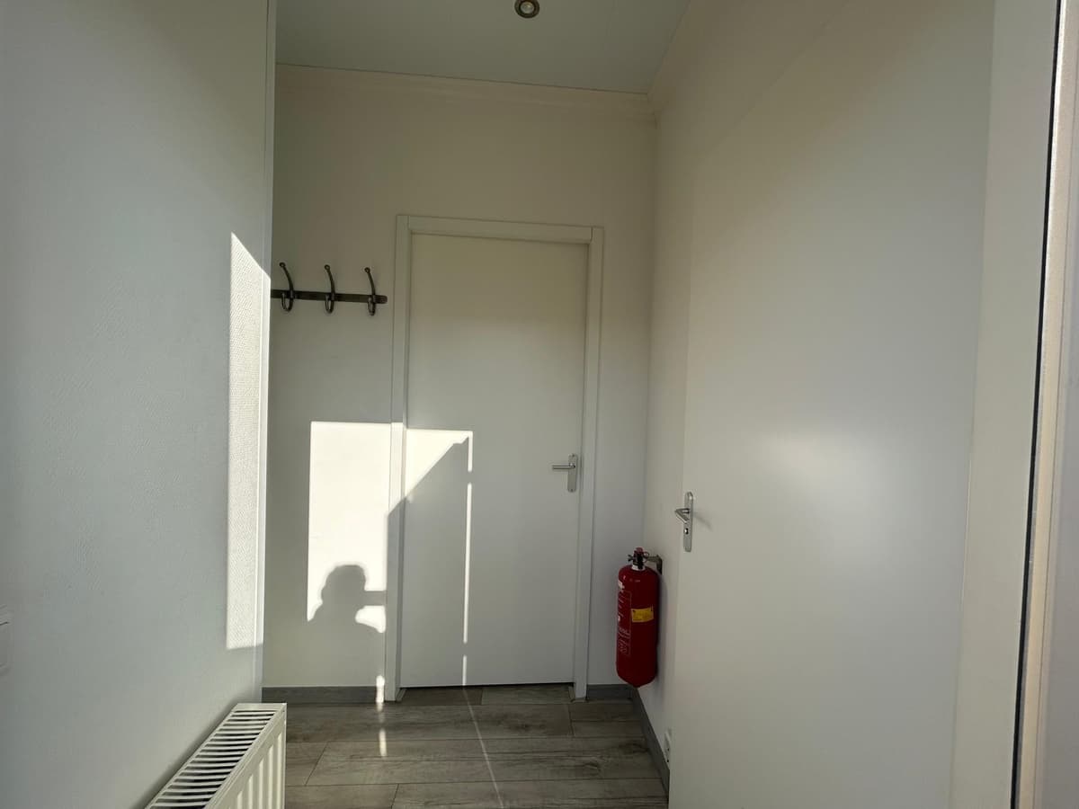 Ingang van de woning met een deur, radiator, haakjes aan de muur en een brandblusser aan de zijkant.
