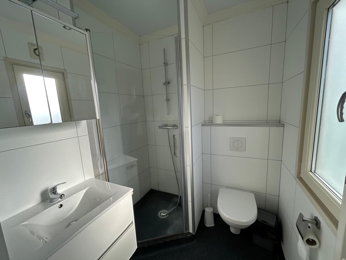 Moderne badkamer met douchecabine, wastafel en toilet in lichte tegelafwerking.