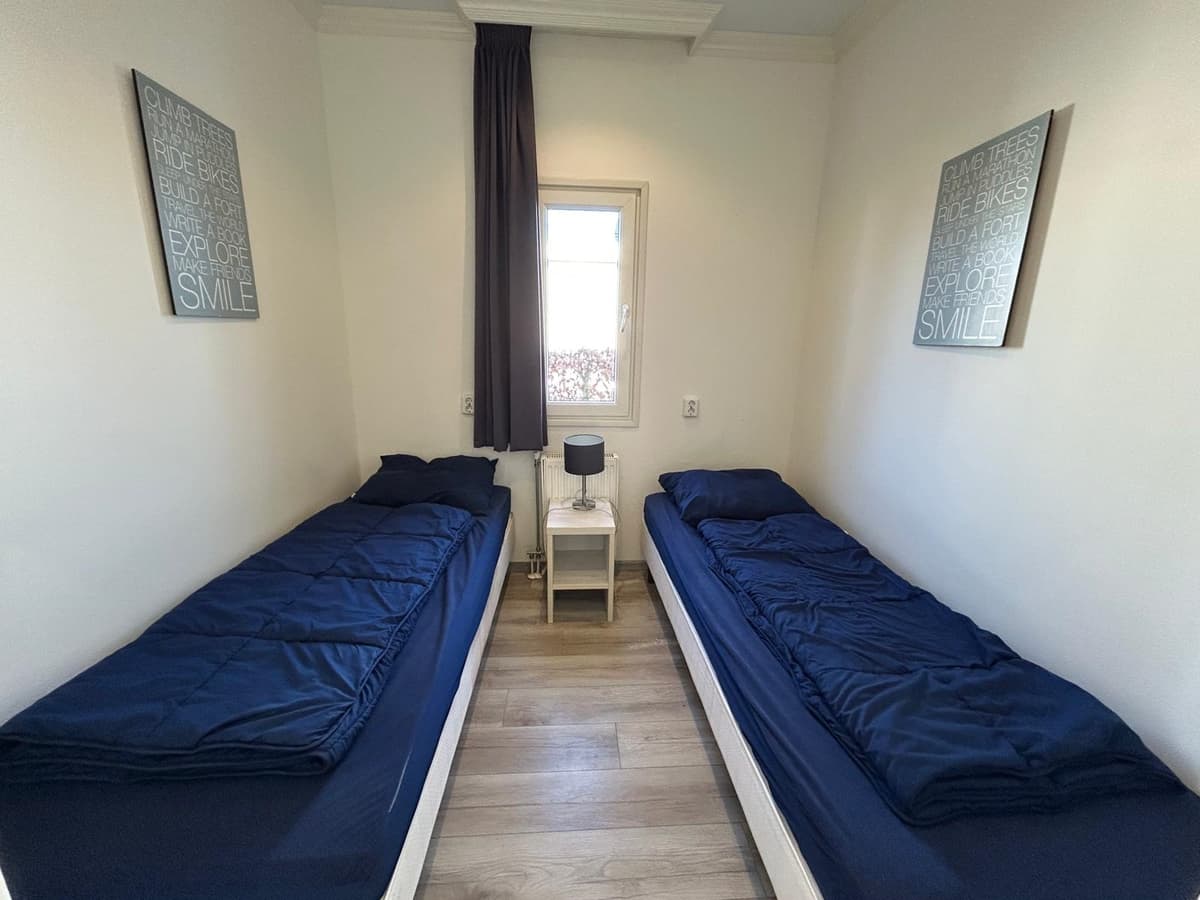 Slaapkamer met twee eenpersoonsbedden, een nachtkastje en een raam met zicht naar buiten