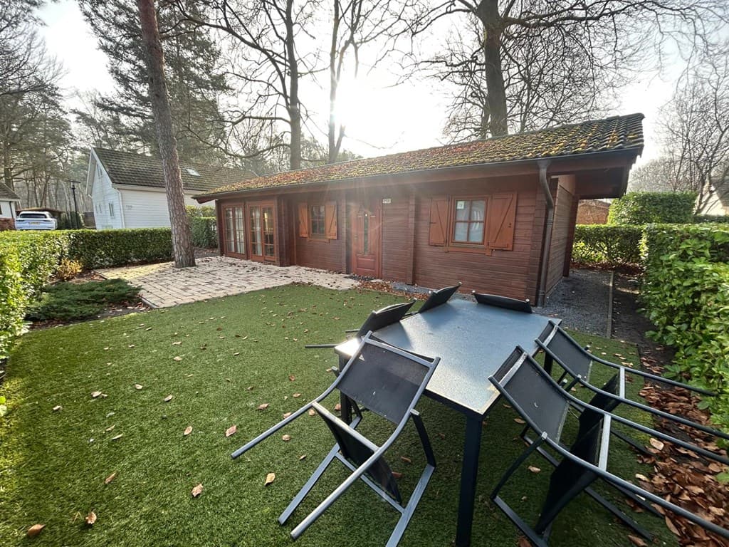 Houten vakantiewoning met tuinmeubilair op het gras en omringd door bomen en haagplanten