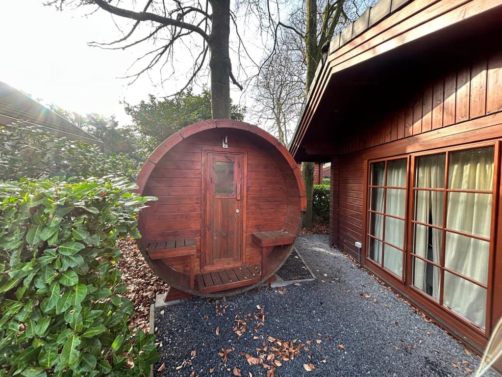 Houten sauna in de tuin, omringd door groen en langs een houten woning met grote ramen