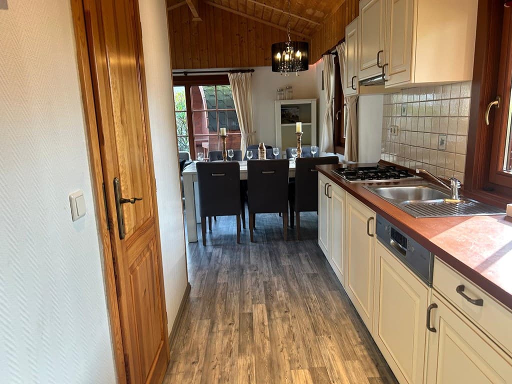 Keuken met houten accenten, die uitkomt op een eetkamer met een grote tafel en uitzicht op de buitenruimte.