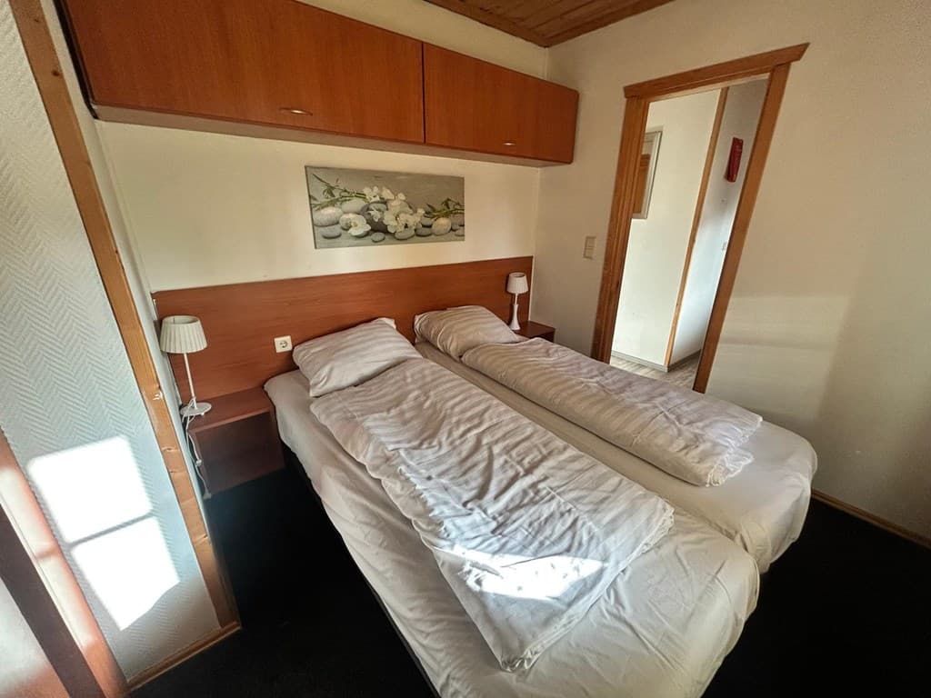 Slaapkamer met twee eenpersoonsbedden, nachtkastjes en wandplanken met bovenverlichting.