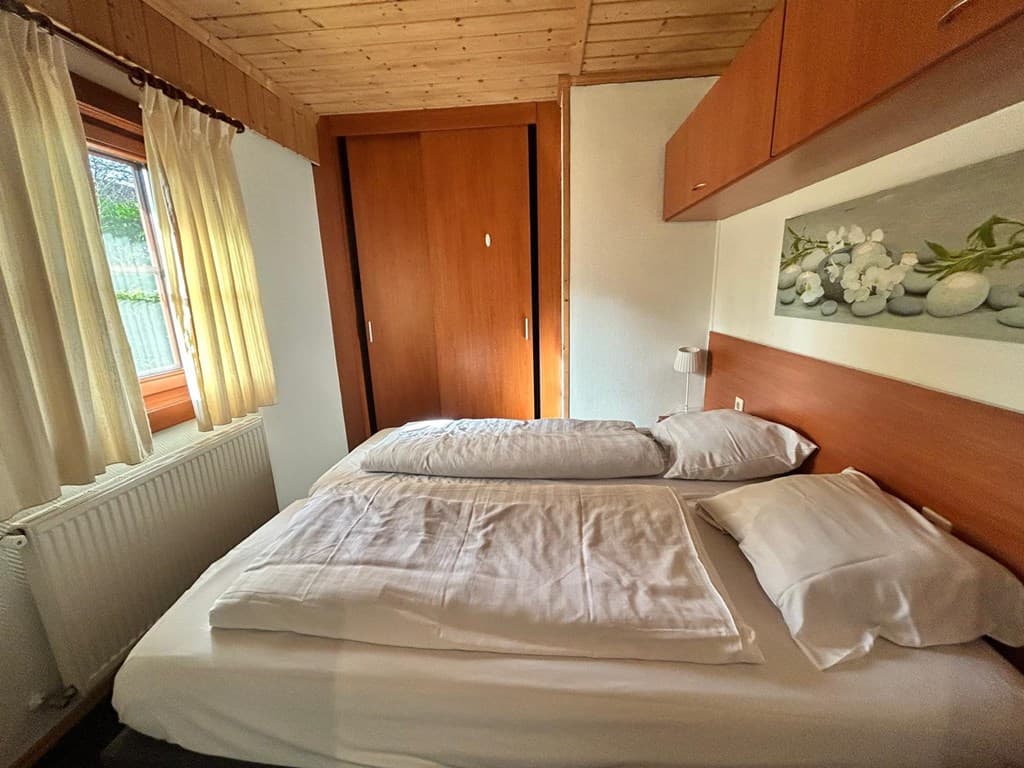 Slaapkamer met twee eenpersoonsbedden, houten plafond en kastruimte, raam met gordijnen en wanddecoratie.