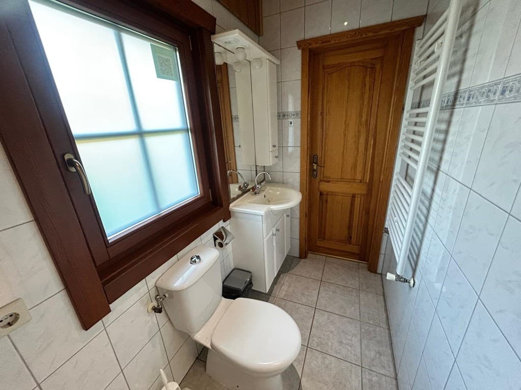 Badkamer met toilet, wastafel en spiegel, betegelde wanden en een houten deur.