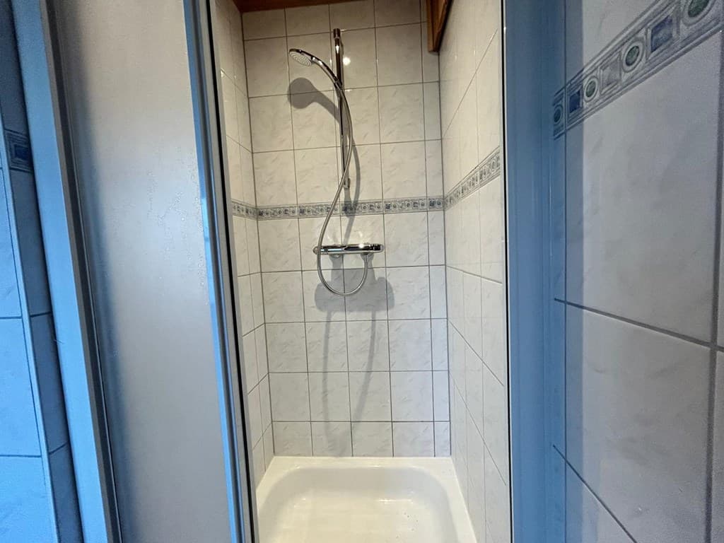 Douchecabine met witte tegels en een doucherail aan de wand