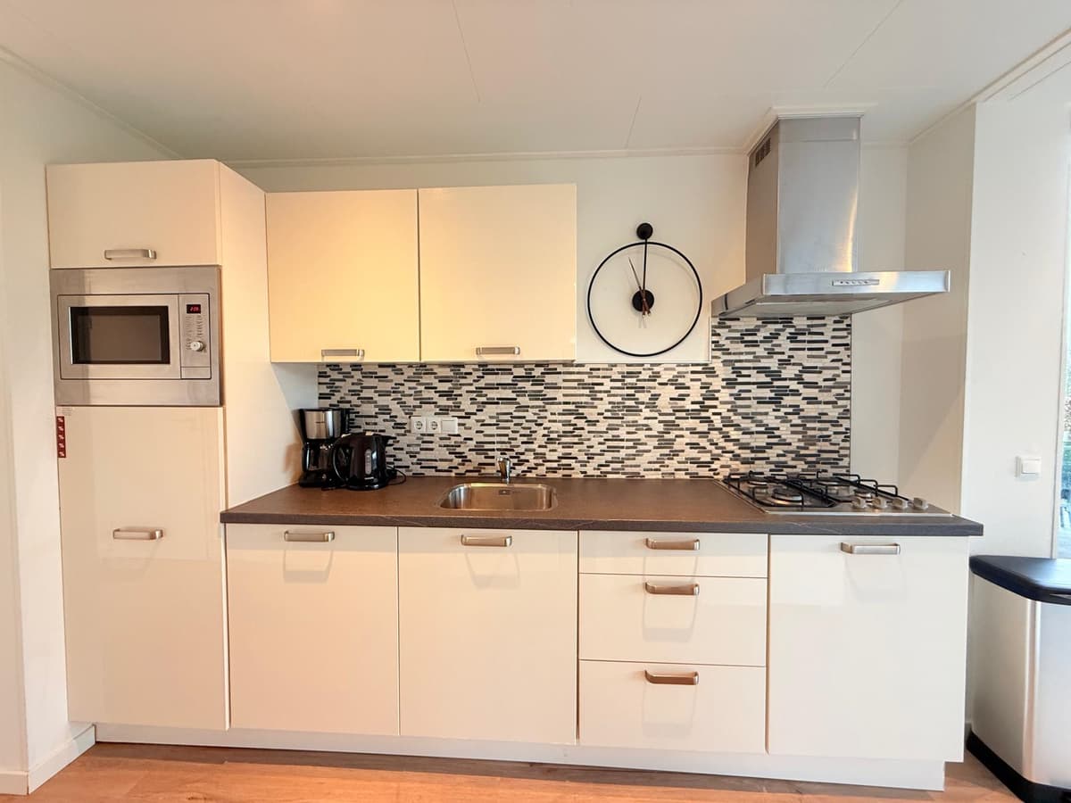 Keuken met moderne inrichting, inclusief oven, kookplaat, afzuigkap en een opvallende betegeling aan de muur