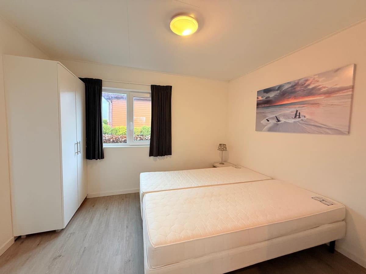 Slaapkamer met twee losse bedden, een kledingkast en een raam met zicht op de buitenruimte.