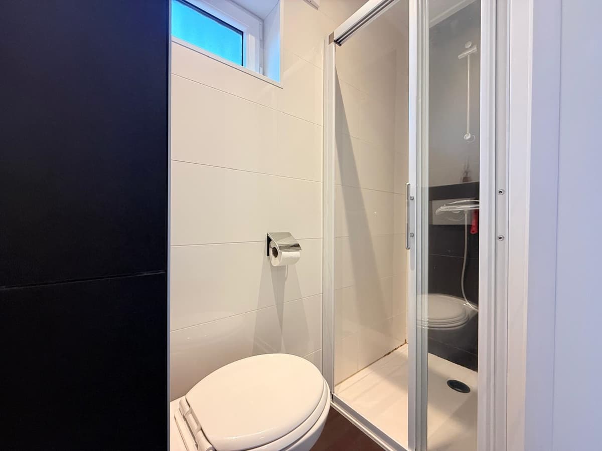 Badkamer met douchecabine, toilet en wastafel, voorzien van witte tegels en een helder raam voor natuurlijk licht