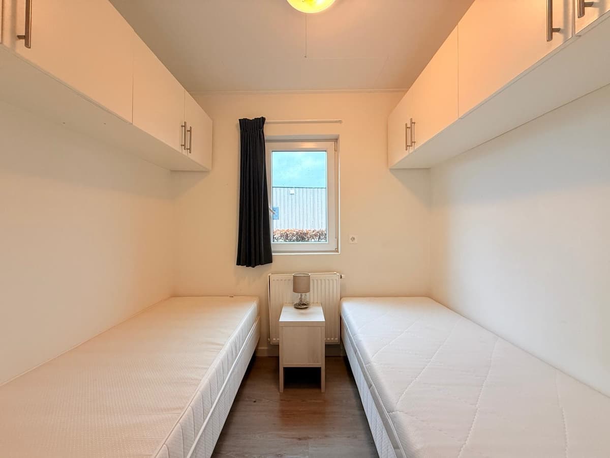 Slaapkamer met twee eenpersoonsbedden, wandkasten en een raam met uitzicht naar buiten.