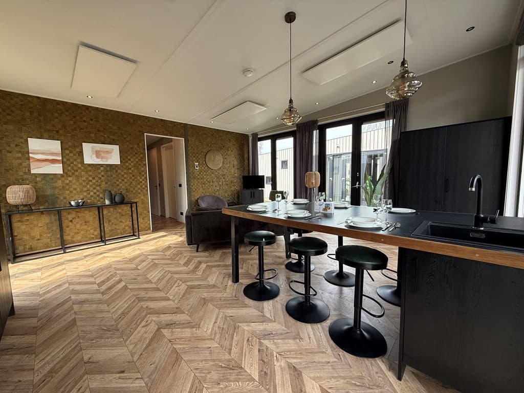 Moderne open keuken met eettafel, hoge krukken en grote ramen met veel natuurlijk licht.