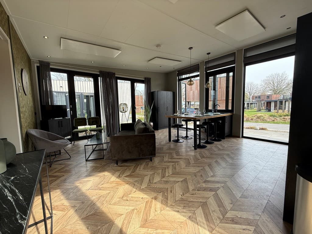Ruime woonkamer met grote ramen, moderne meubels en een open keuken in EuroParcs Kaatsheuvel.