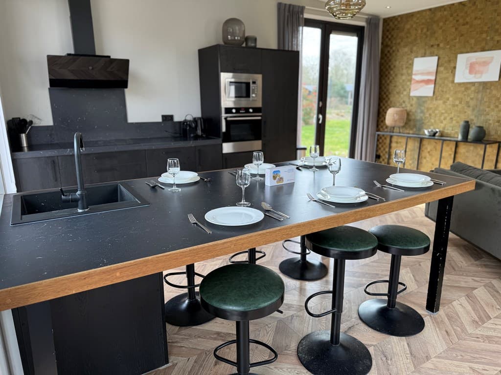 Moderne keuken met een eetbar, zwarte afwerking, vier stoelen en uitzicht op de tuin door dubbele deuren.