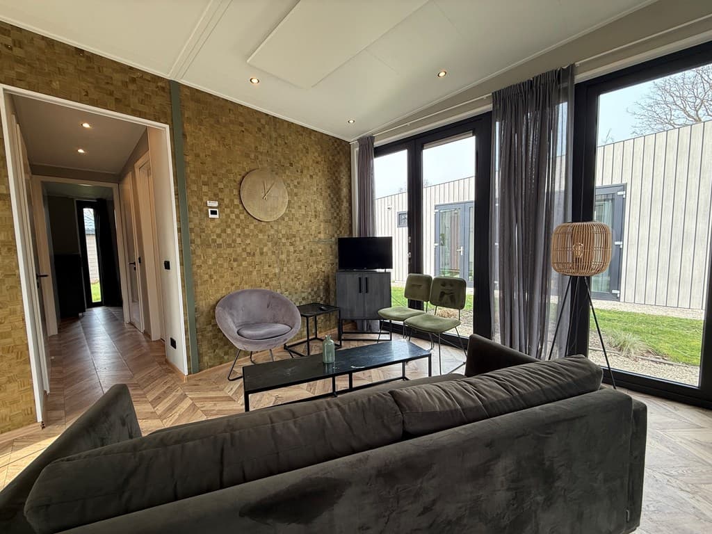 Moderne woonkamer met grote ramen, comfortabele zitmeubels en een eettafel, bij EuroParcs Kaatsheuvel.