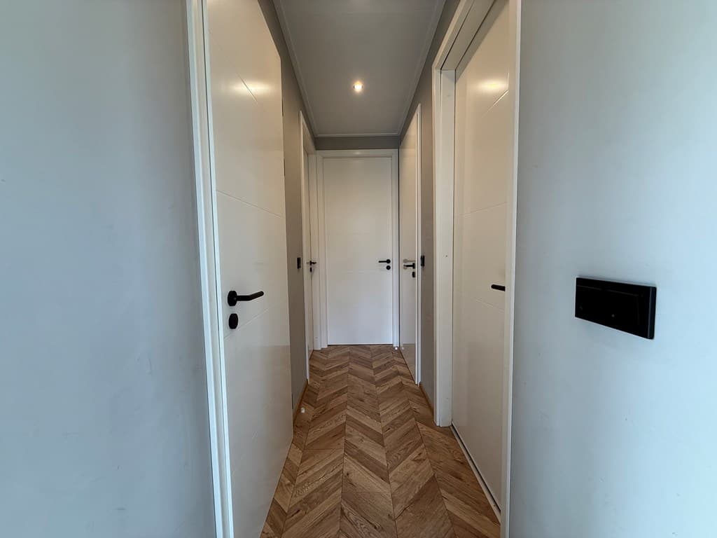 Dubbele gang in een modern interieur met houten visgraatvloer en verschillende deuren aan beide zijden