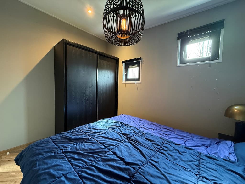 Slaapkamer met een donker kledingkast, blauwe dekbedovertrek en een moderne hanglamp aan het plafond.
