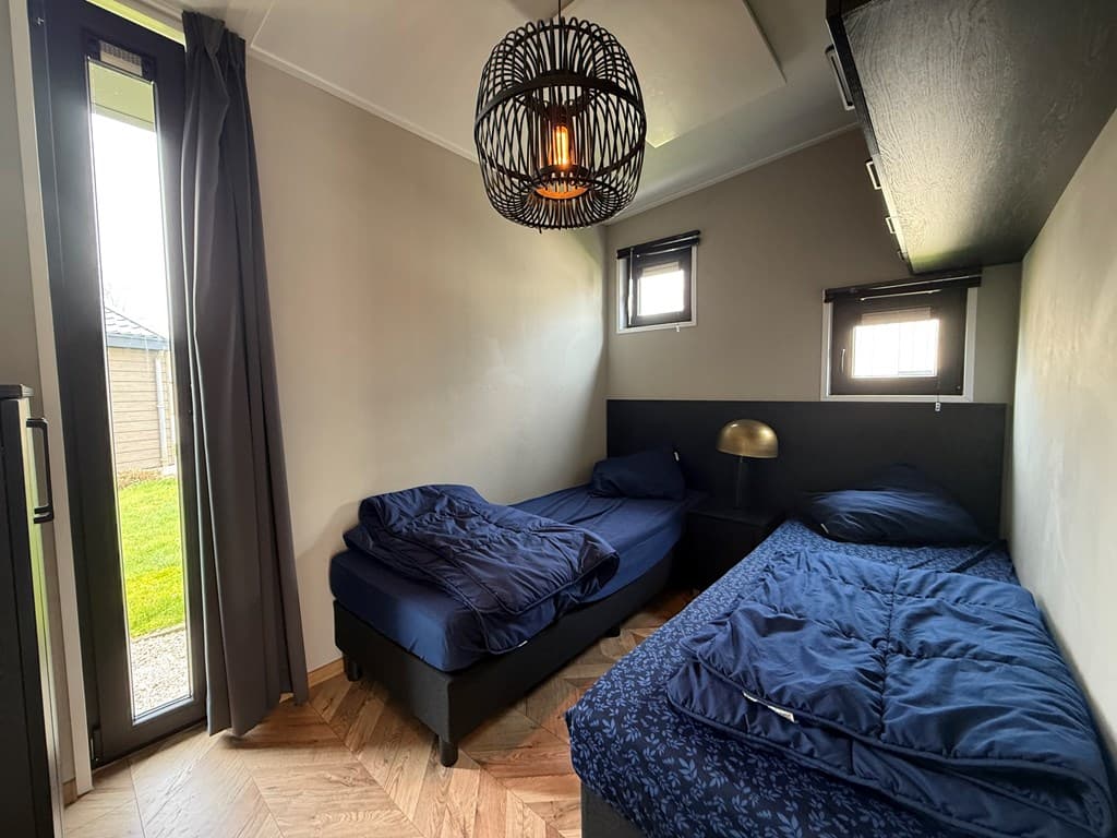 Slaapkamer met twee eenpersoonsbedden, nachtkastje en een deur naar de tuin met zicht op gras.