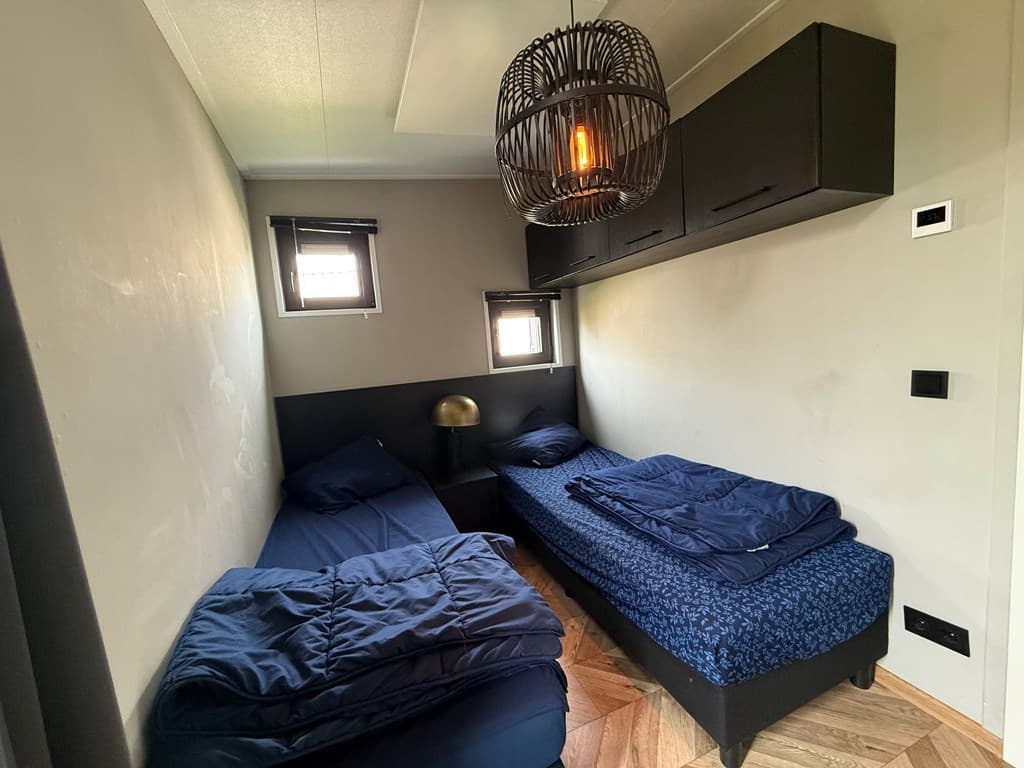 Slaapkamer met twee eenpersoonsbedden, wandkast en een hanglamp met een natuurlijk design.