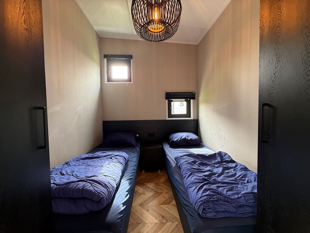 Slaapkamer met twee eenpersoonsbedden, houten vloeren en een moderne lamp aan het plafond.