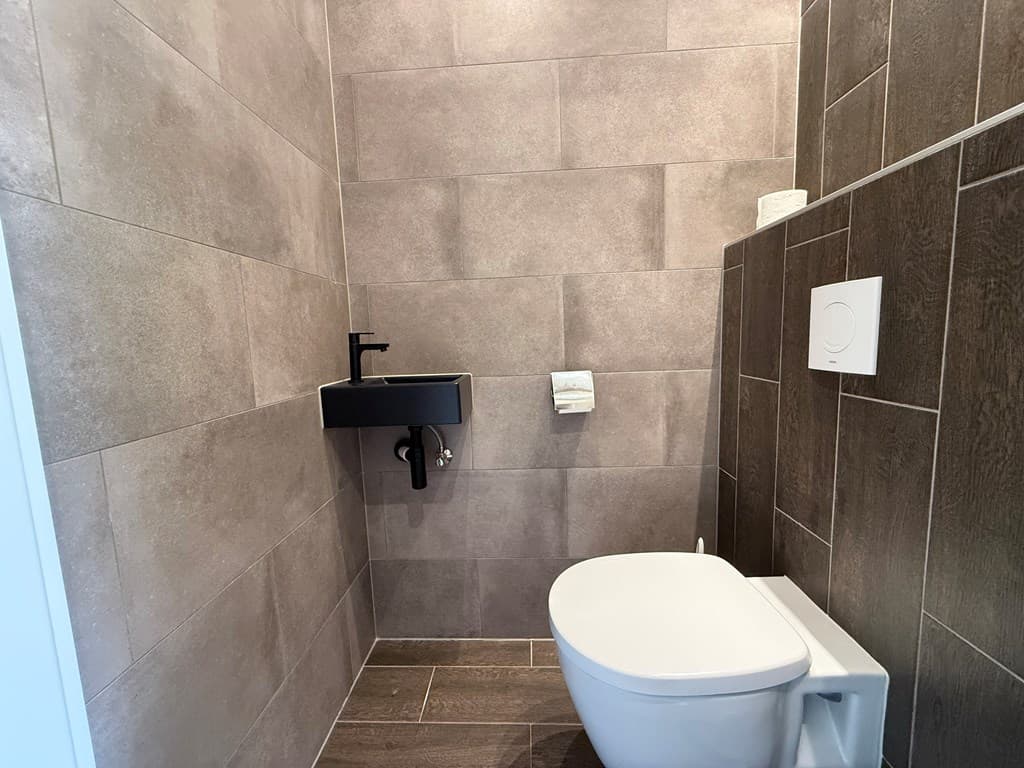 Lichte moderne toiletruimte met tegelwanden, een wandcloset en een klein wastafelmeubel.