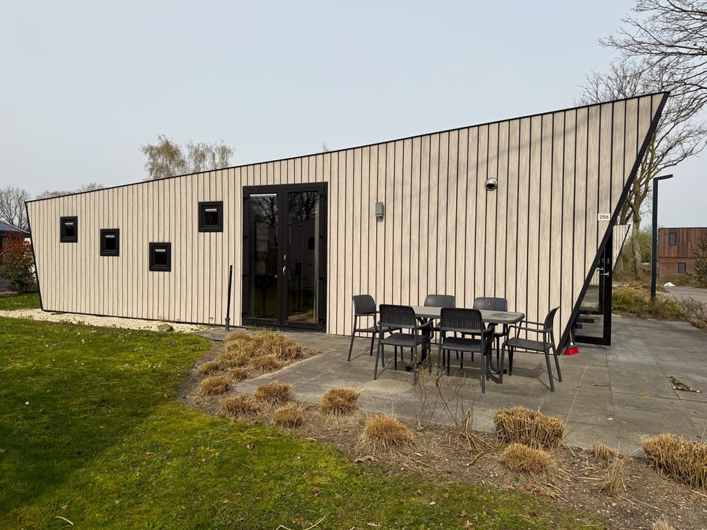 Moderne vakantiewoning met een schuin design, terras en tuinmeubelen op een betegeld pad in een groene omgeving