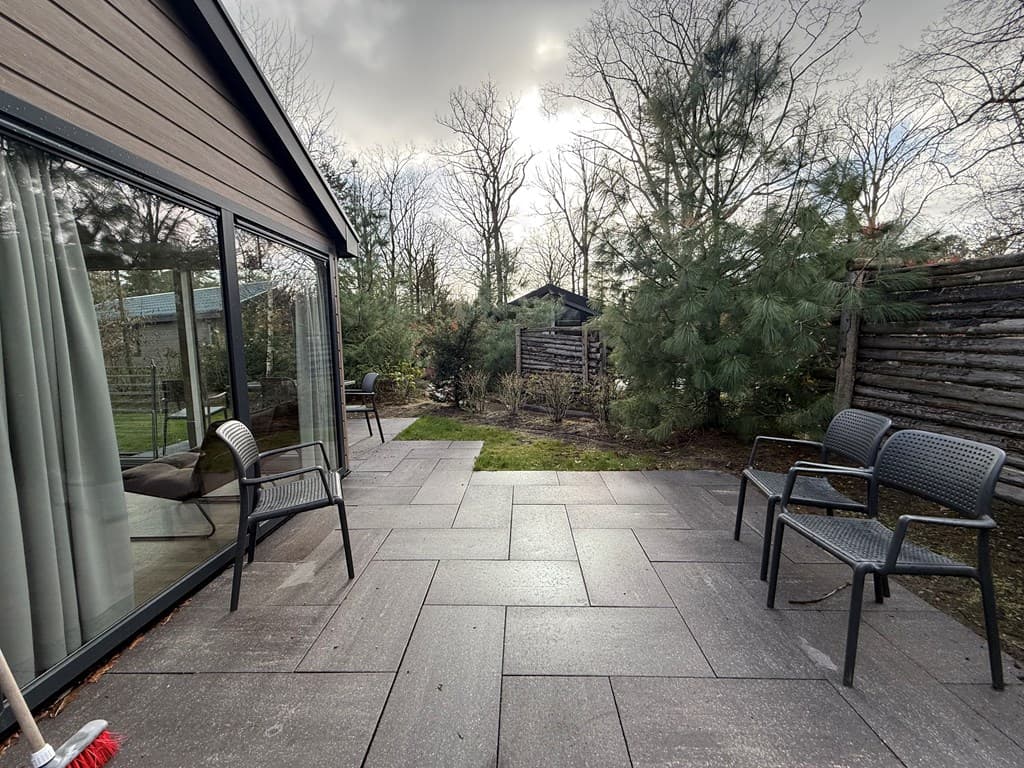 Terras met tegels, omringd door planten en bomen, en enkele stoelen met uitzicht op een tuin en een houten schutting