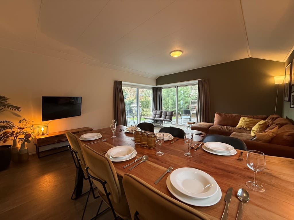 Gezellige woonkamer met eettafel, aangrenzende zithoek en grote ramen met uitzicht op de tuin.