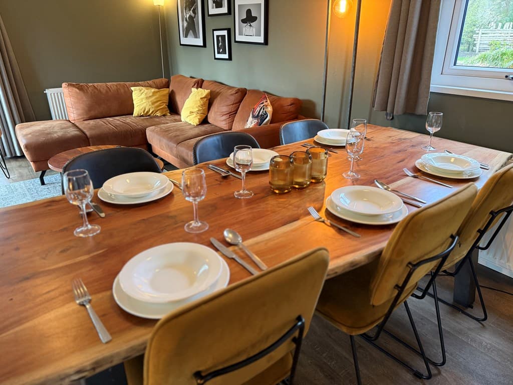 Eettafel met servies, glazen en bestek, naast een zithoek met een grote bank en decoratieve foto's aan de muur.