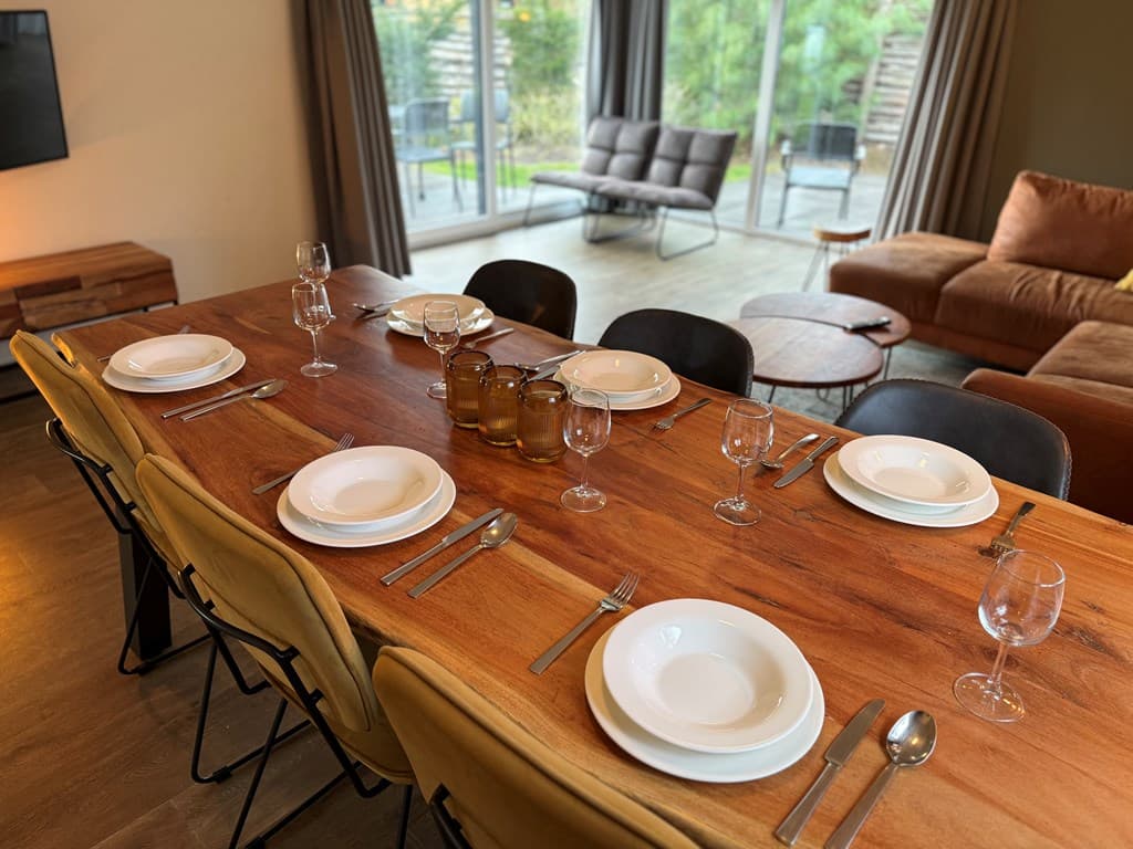 Eettafel met servies voor acht personen en uitzicht op tuin door grote glazen schuifpui