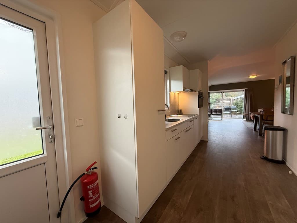 Moderne keuken met kastjes, deur naar buiten, en open verbinding naar de woonruimte met tafel en stoelen.