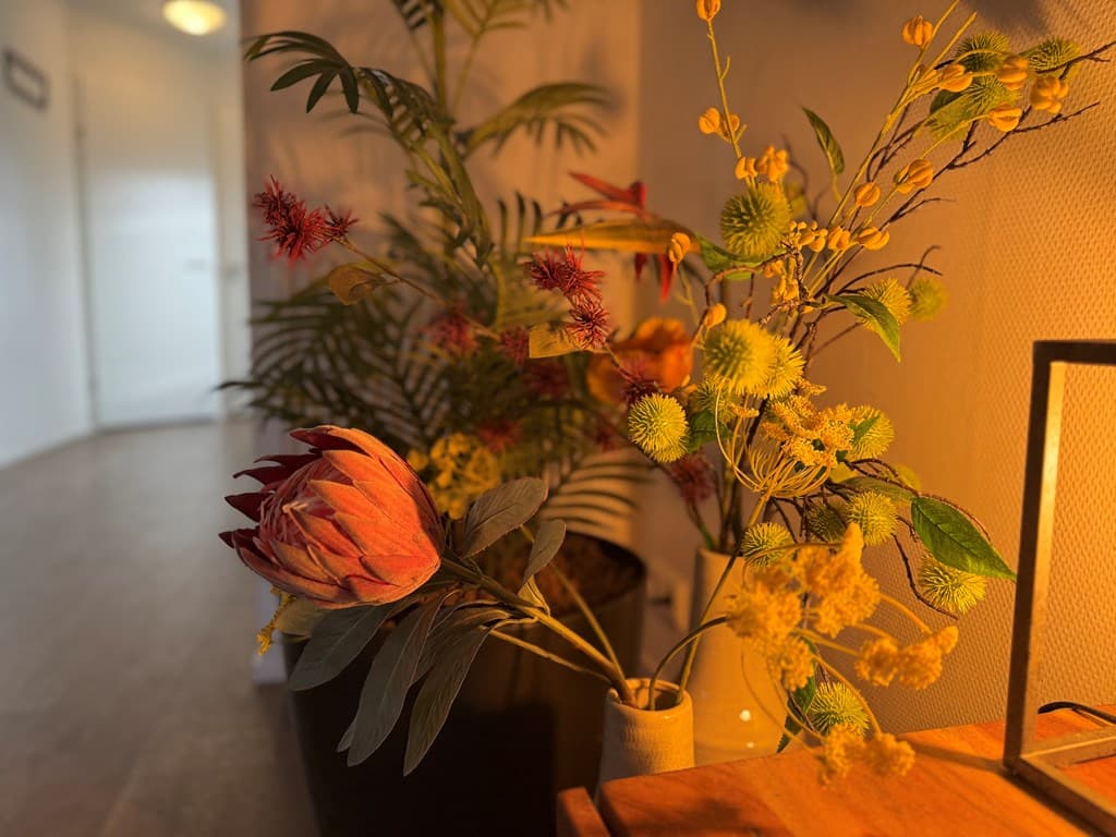 Fleurige kunstbloemen en planten in een pot op een houten tafel met warme verlichting in een moderne ruimte.