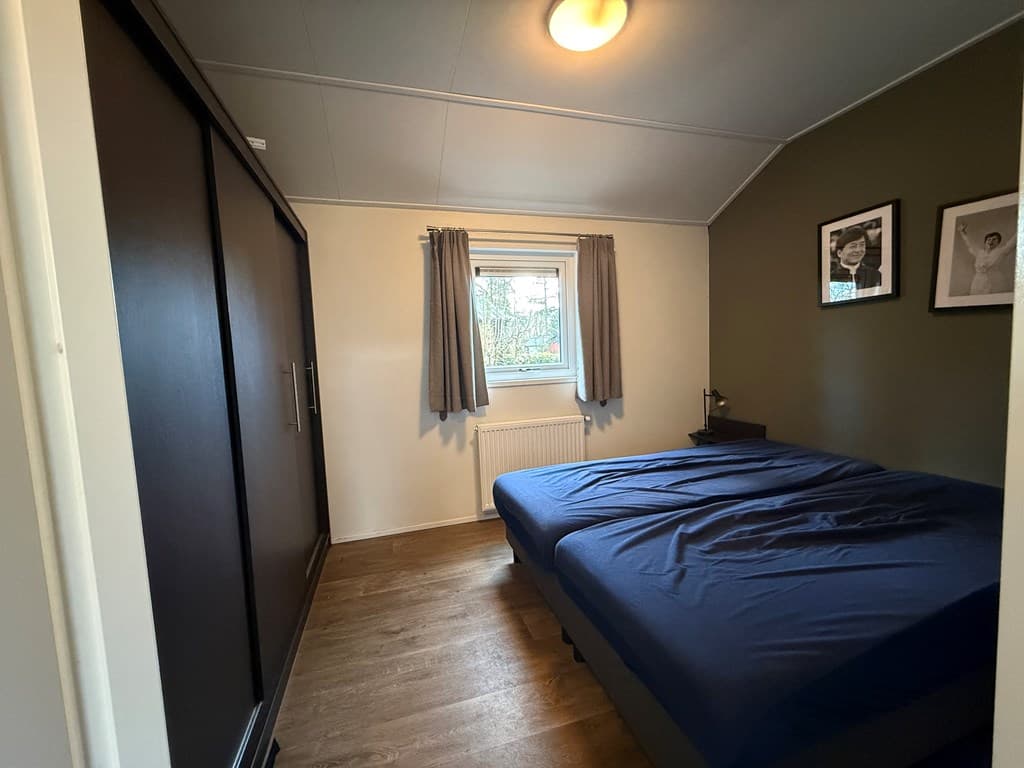 Slaapkamer met een bed, kast, raam en enkele ingelijste foto's aan de muur