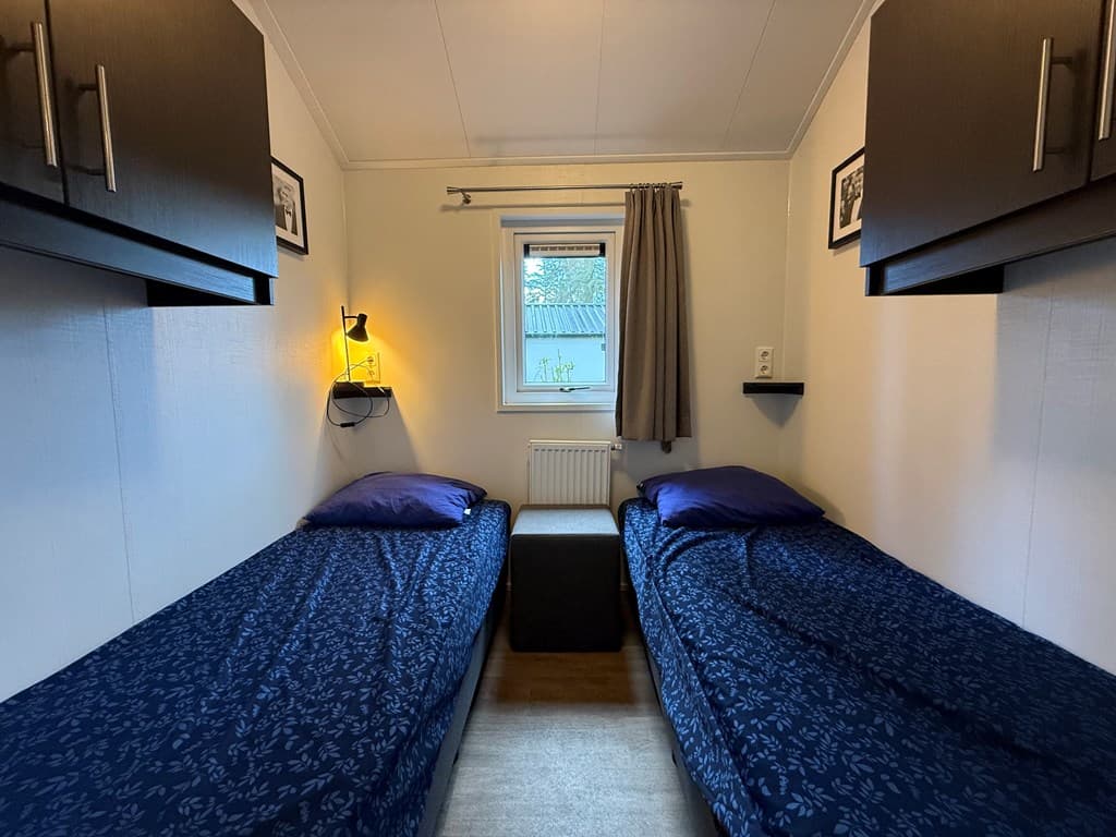 Slaapkamer met twee eenpersoonsbedden, een nachtkastje en verlichting aan de wand.