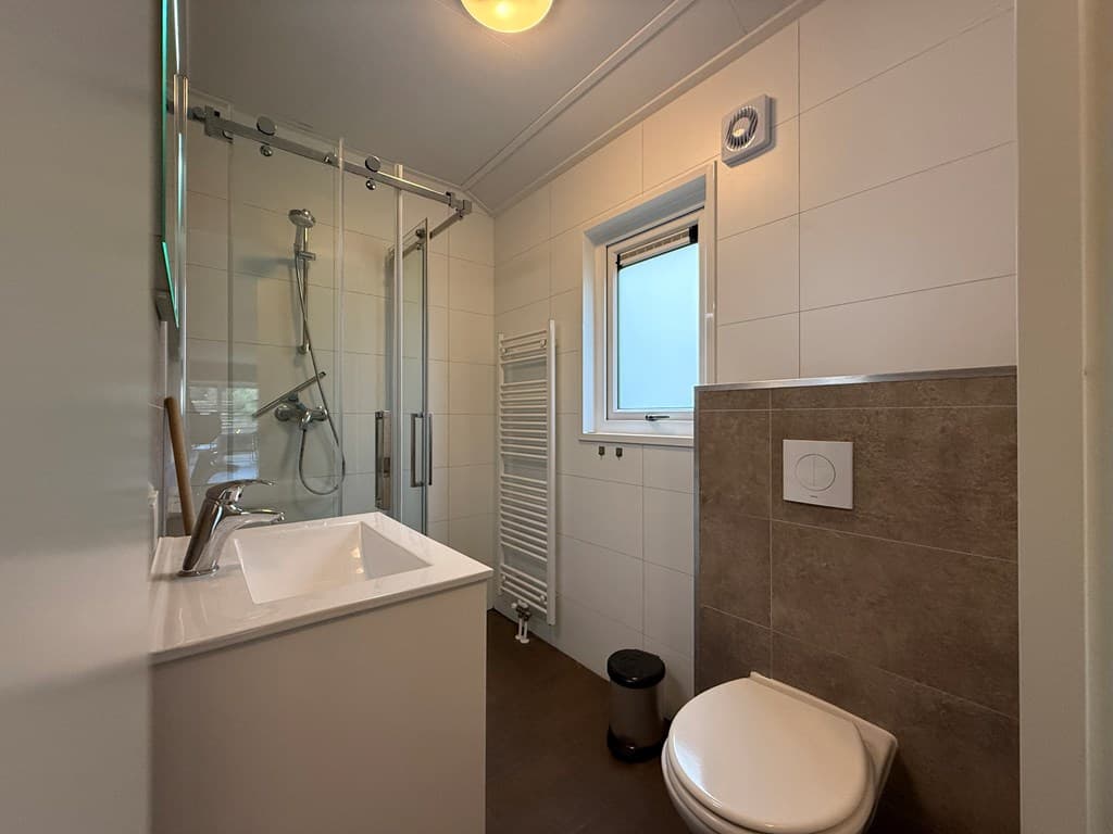 Moderne badkamer met douche, wastafel en toilet, tegels in lichte en donkere kleur, en een handdoekenrek.